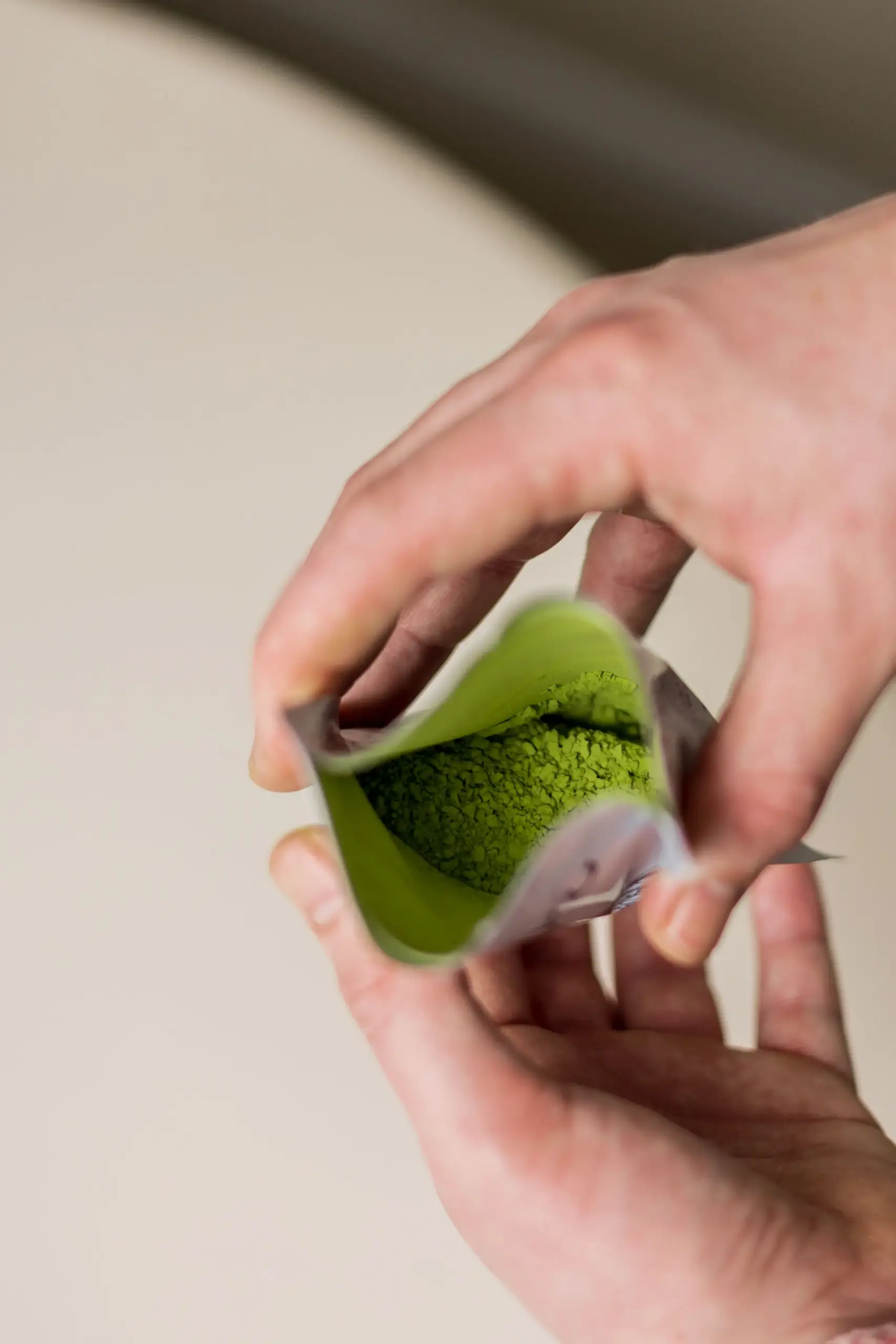 Handen die een geopend zakje met helder groen matchapoeder vasthouden