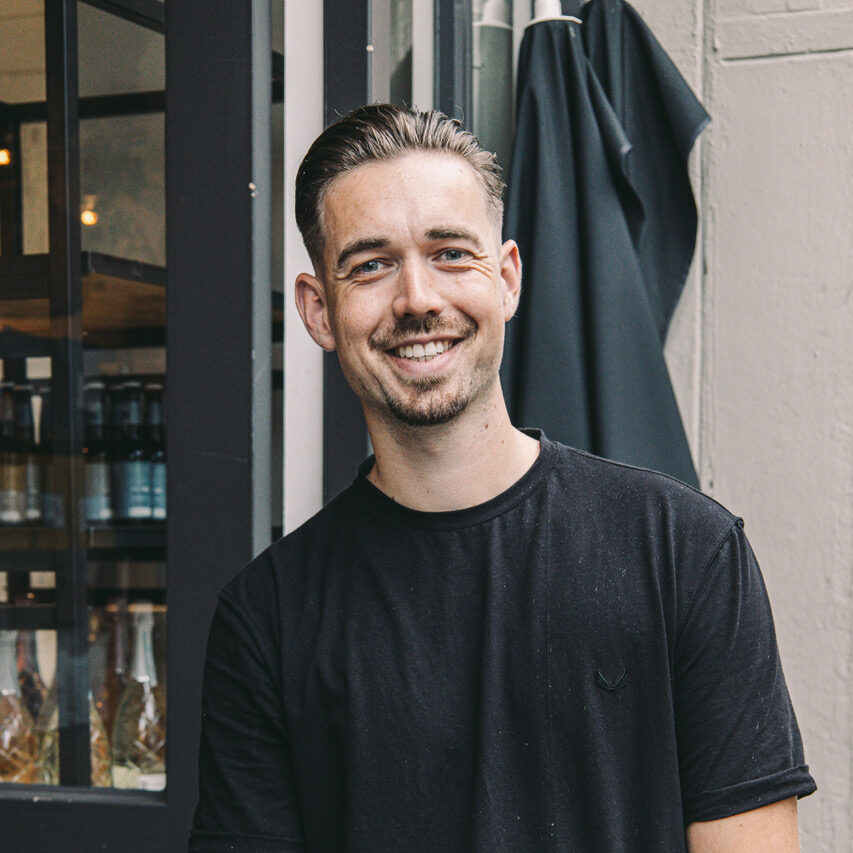 Smiling young man in a black t-shirt standing outside a bar or restaurant
