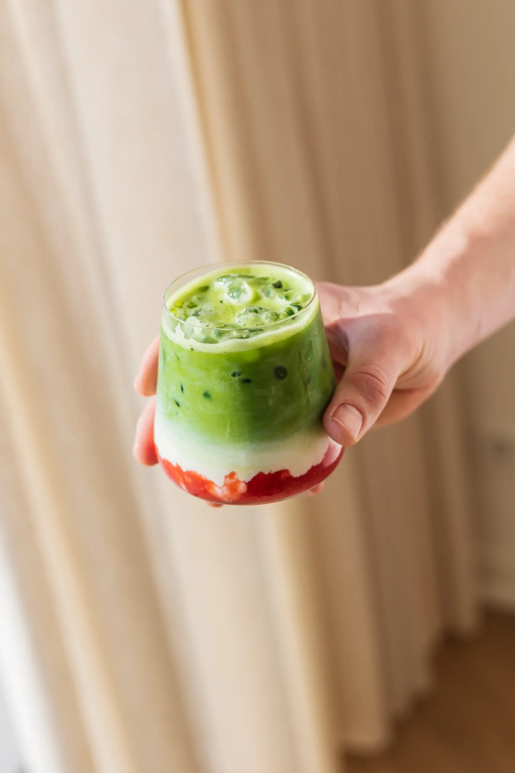 SHINYU Matcha - Membership 6 Hand houdt een glas vast met gelaagde iced matcha latte met aardbeien en melk onderaan