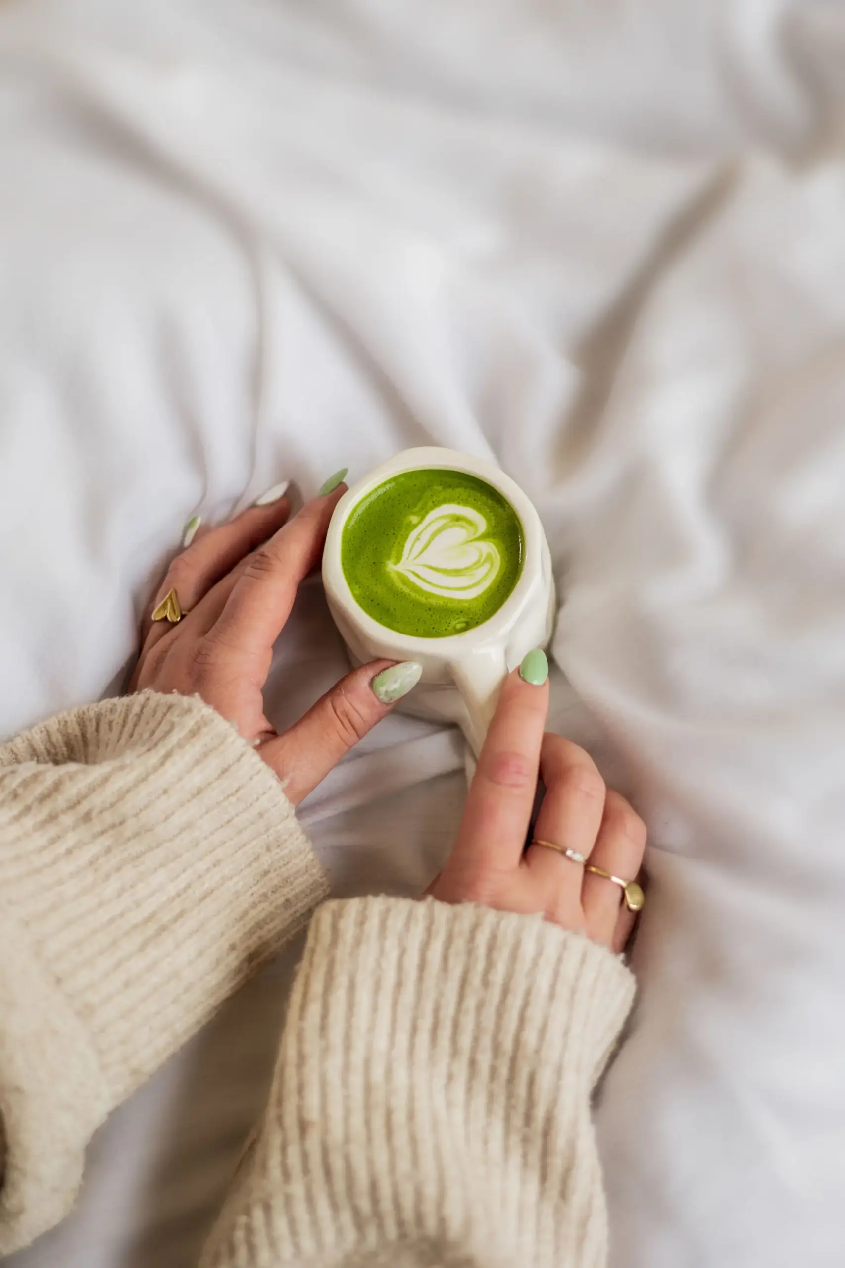 SHINYU Matcha Six Pack (6x30gr) 5 Hands cradling a matcha latte with latte art in a white ceramic mug on white bedding