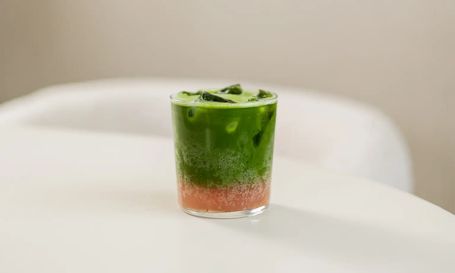Gelaagd ijskoud drankje met groene matcha bovenop een roze laag, geserveerd in een glas met ijsblokjes