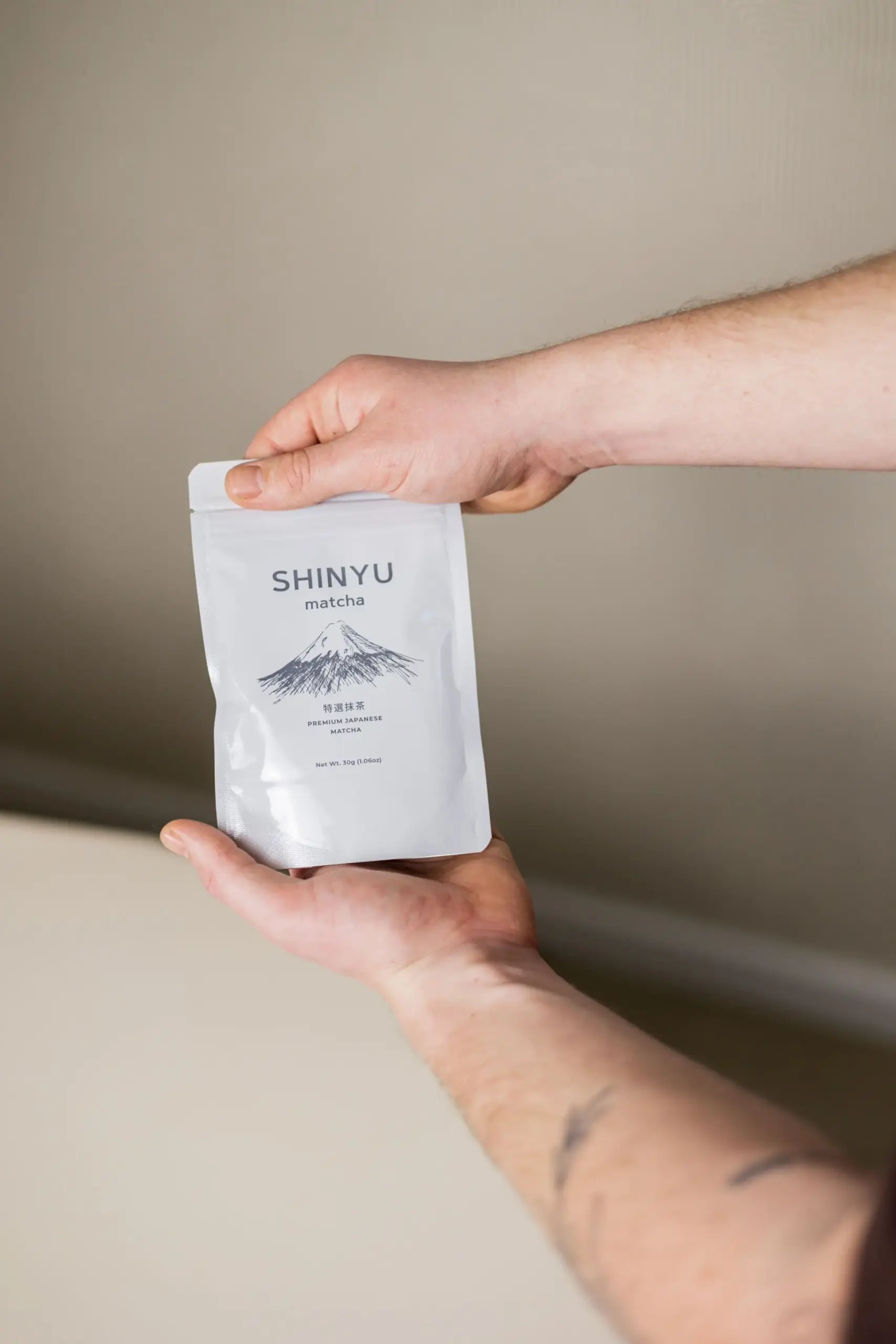 SHINYU Matcha - Single pack (30gr) 6 Hands holding a white pouch of Shinyu Matcha Premium Japanese Matcha, 30g, featuring an illustration of Mount Fuji