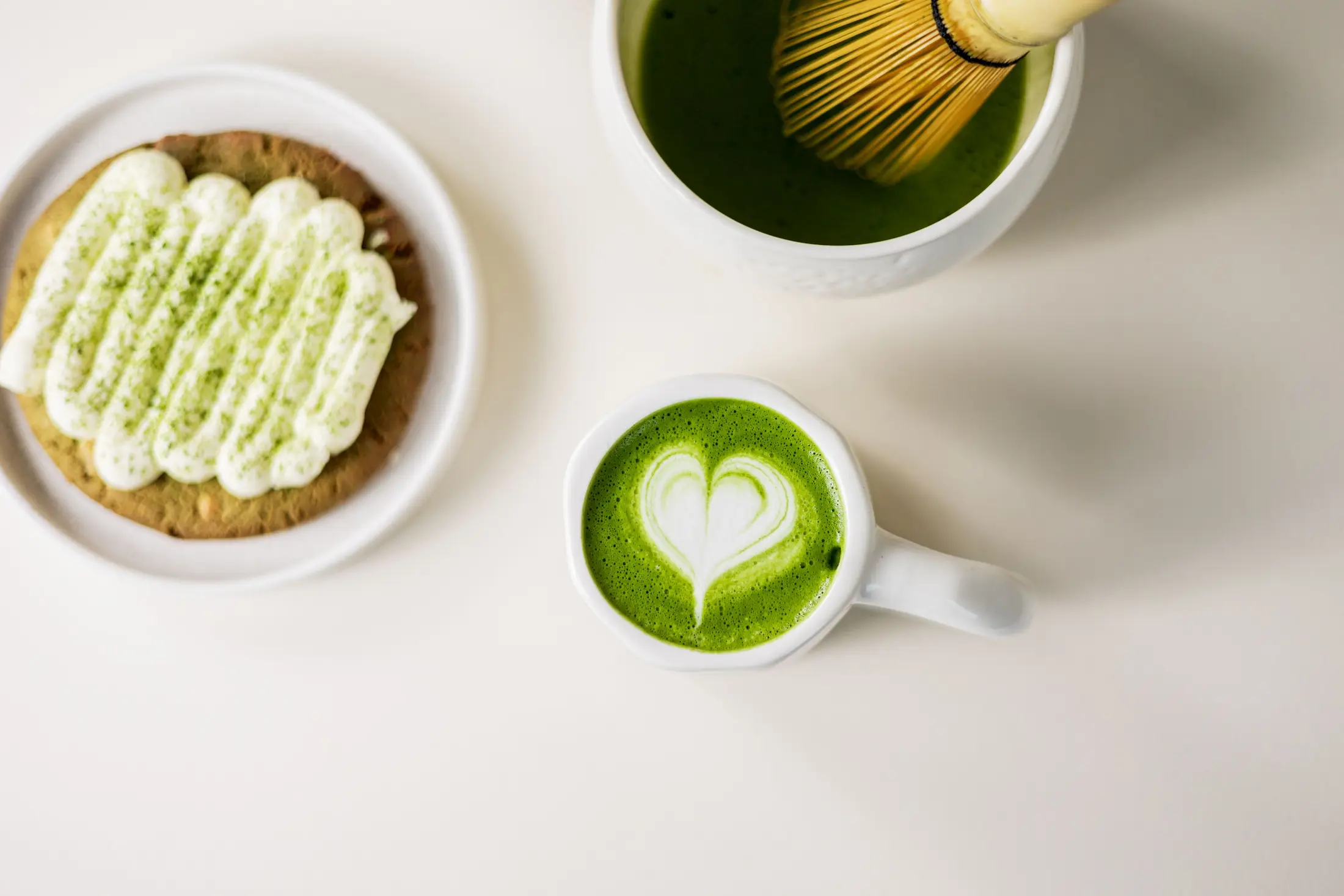 Matcha latte met hartvormige latte art, een koekje met matcha glazuur en een kom matcha met klopper