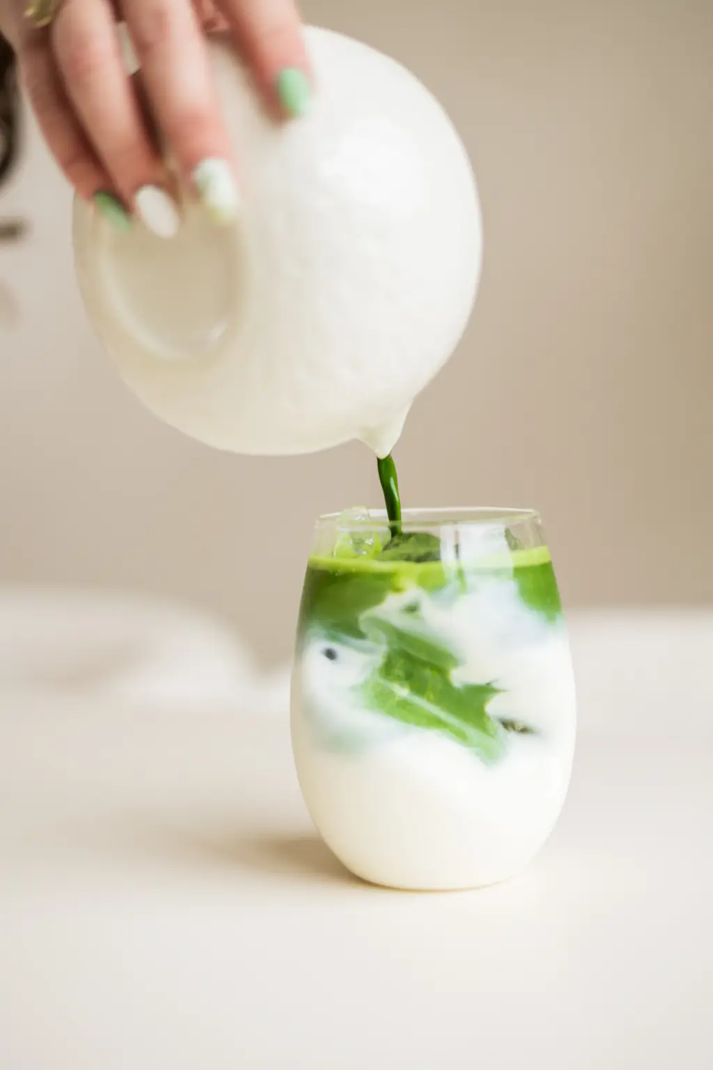 Matcha wordt gegoten in een glas met melk en ijsblokjes, waardoor een swirl van groen en wit ontstaat