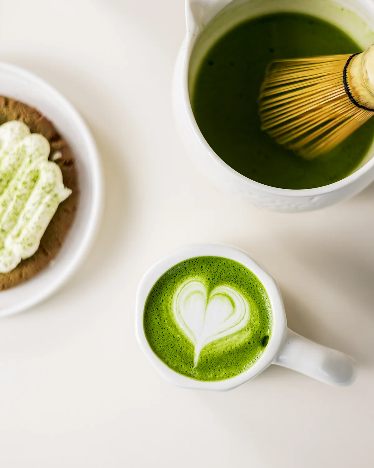 Matcha latte met hartvormige latte art, een kom matcha met bamboe klopper en een koekje met slagroom