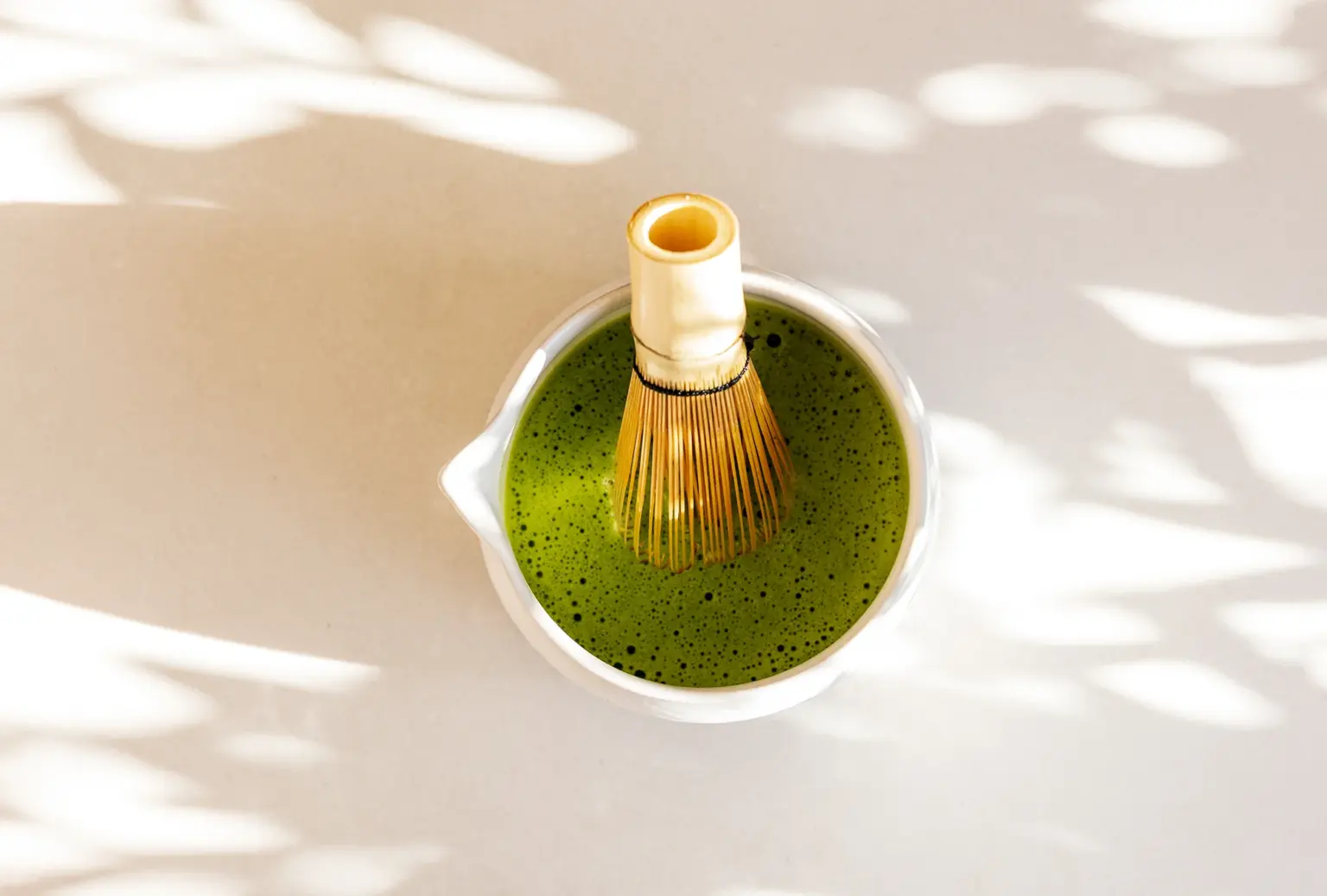 Bamboe matcha-klopper in een witte kom met schuimende groene matcha thee, van bovenaf gefotografeerd