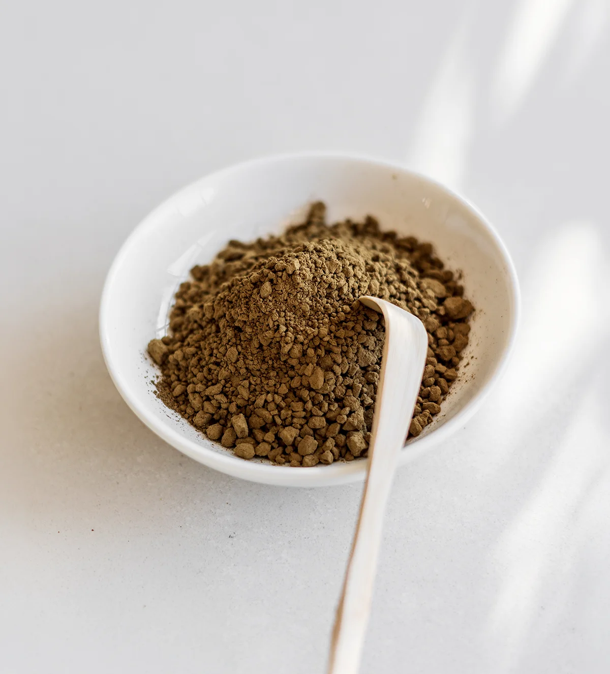 SHINYU Hojicha - 10x30gr 2 Small white bowl filled with earthy green-brown powder, with a wooden spoon resting inside, on a white surface