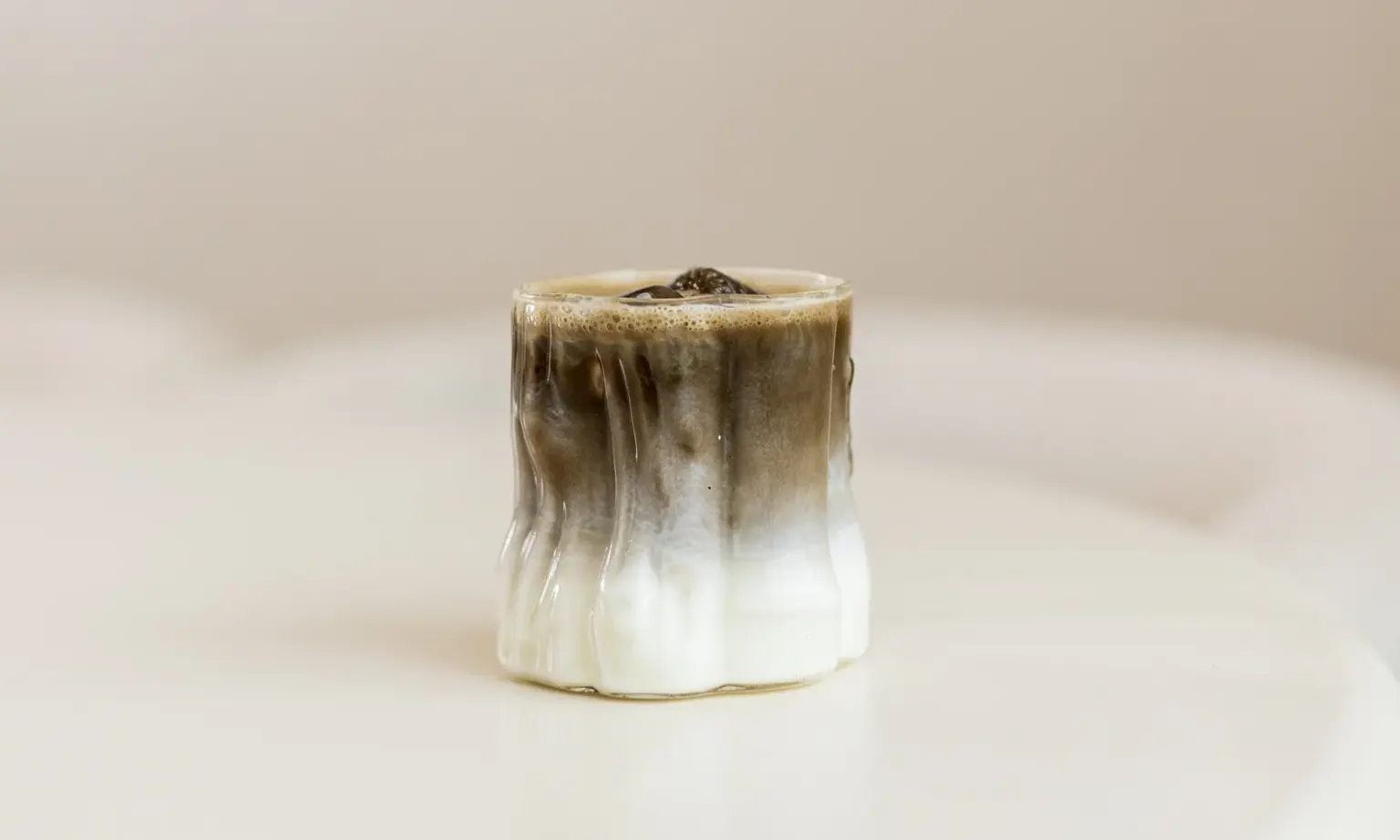 IJskoffie met melk in een geribbeld glas, met zichtbare lagen van witte melk en donkere koffie