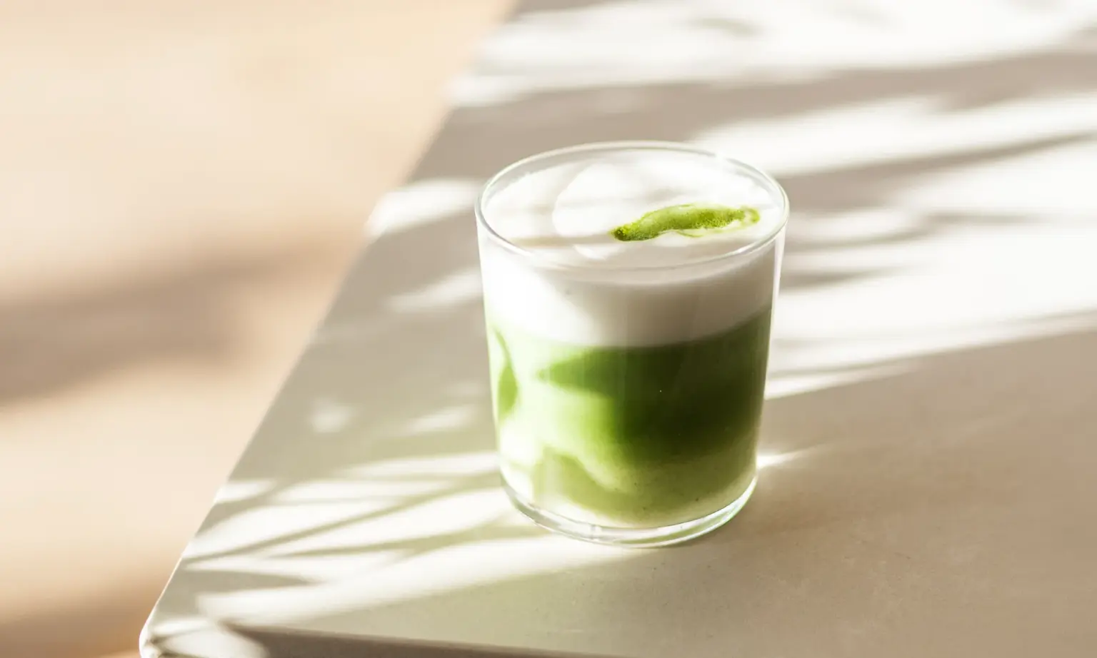 Matcha latte in een glazen beker met melkschuim en een snufje matcha poeder, in zonlicht