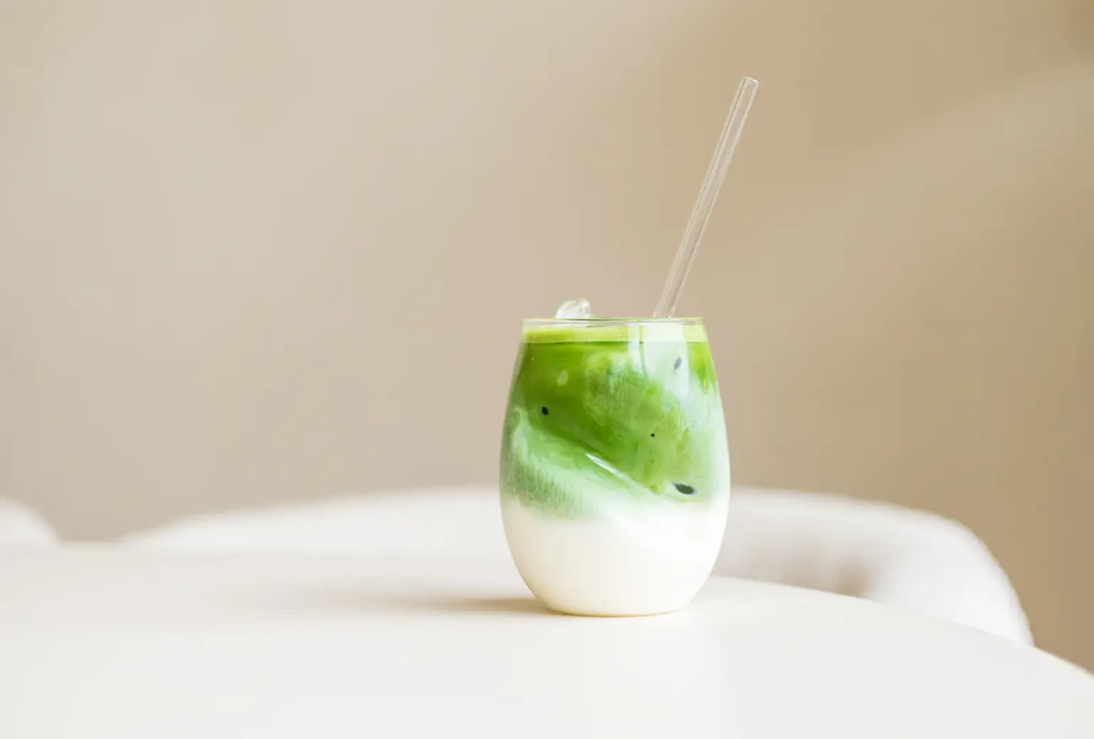 IJskoude matcha latte in een glazen beker met een glazen rietje, met wervelende groene en witte lagen