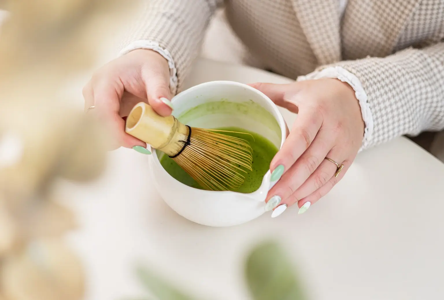 Vrouw klopt matcha thee met een bamboeklopper in een witte kom