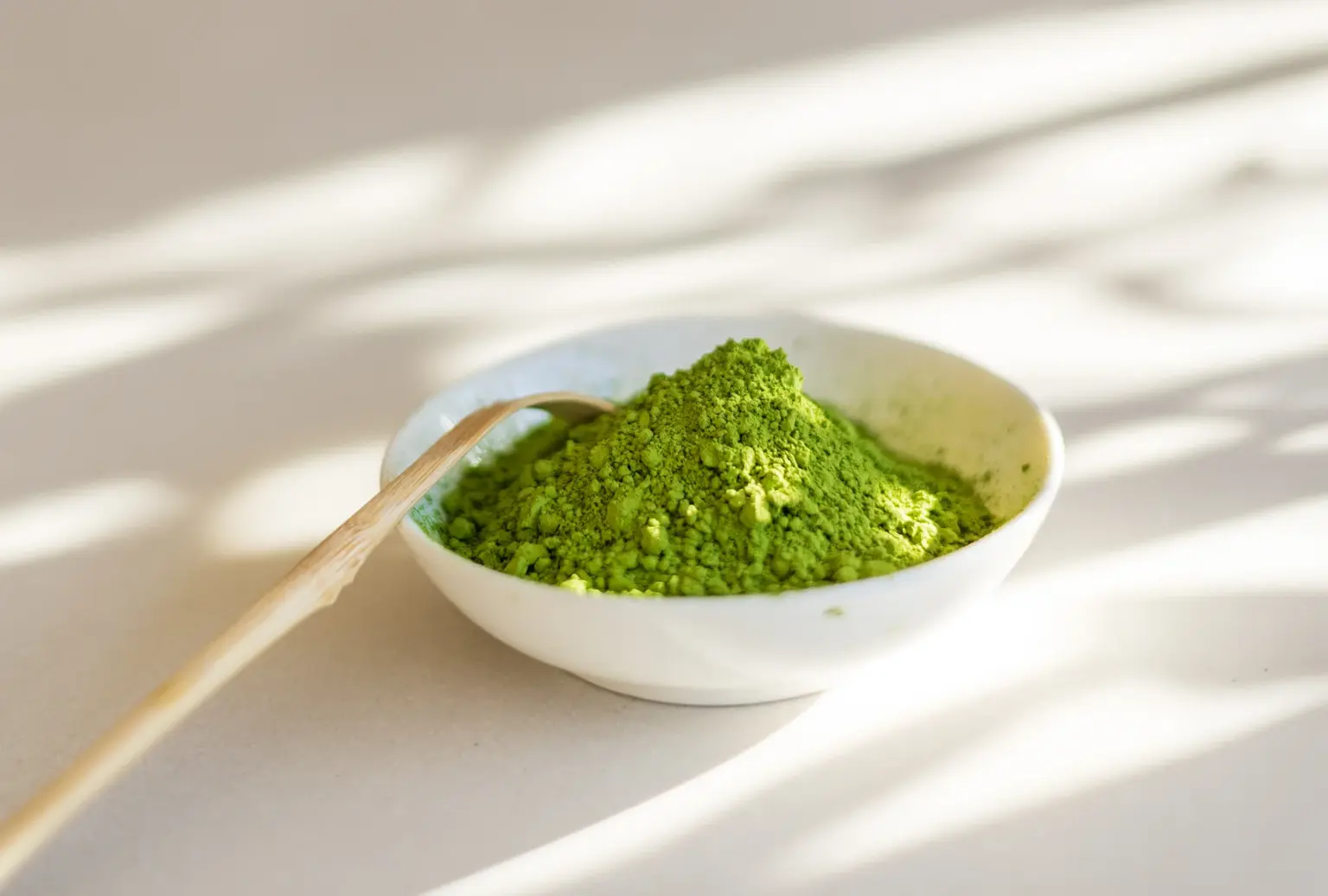 Levendig groen matchapoeder in een wit kommetje met een bamboeen lepel, in natuurlijk zonlicht