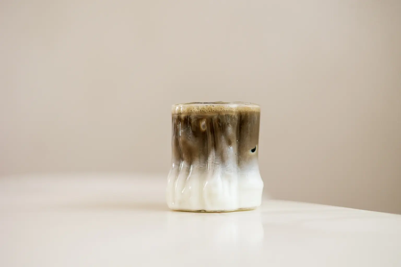 Handgemaakte keramieke kop met bruine en witte druipglazuur, gevuld met koffie met schuim