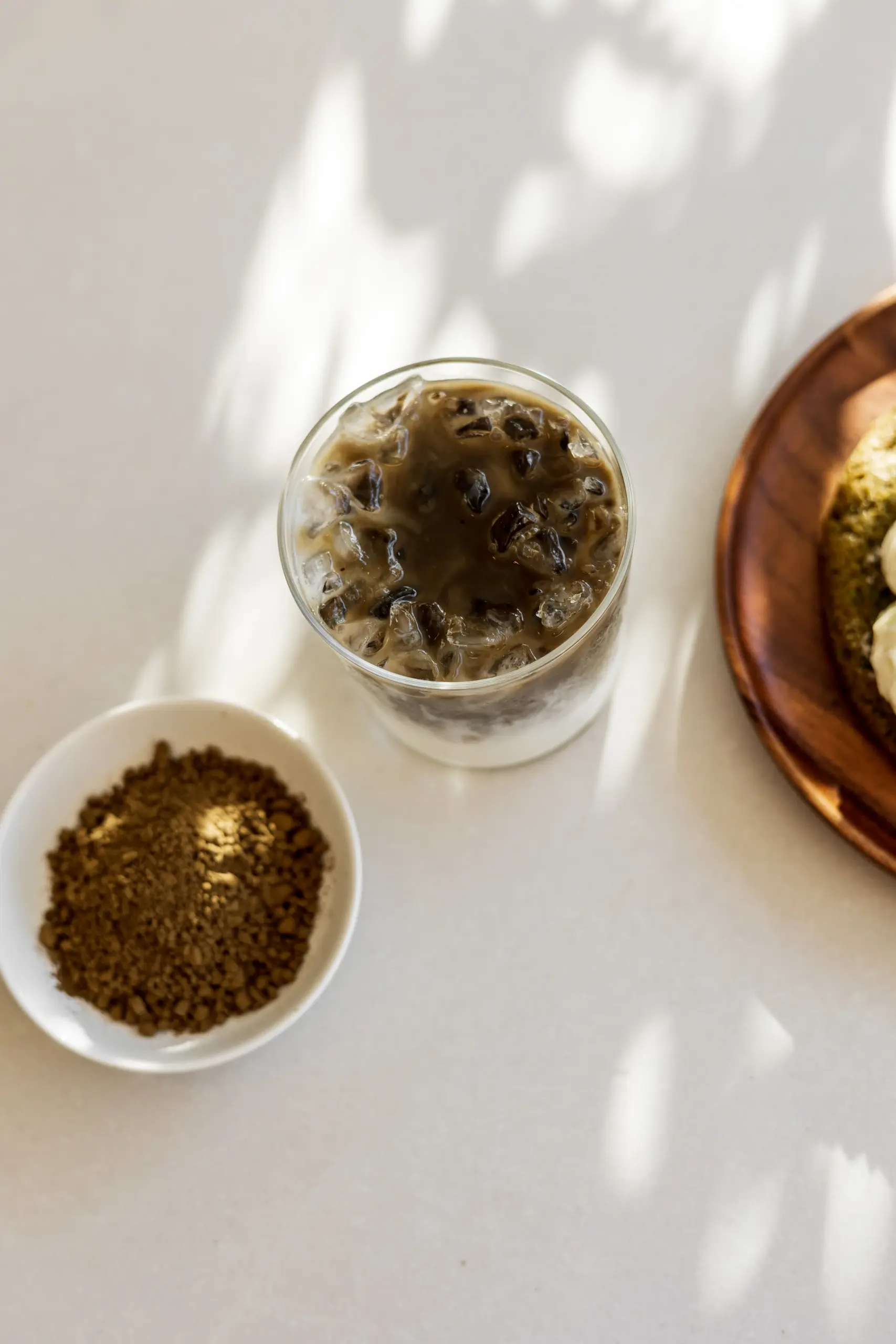 SHINYU Hojicha - large pack - 1 kilo 3 Iced coffee in a glass next to a small bowl of ground coffee, with a wooden plate of food partially visible