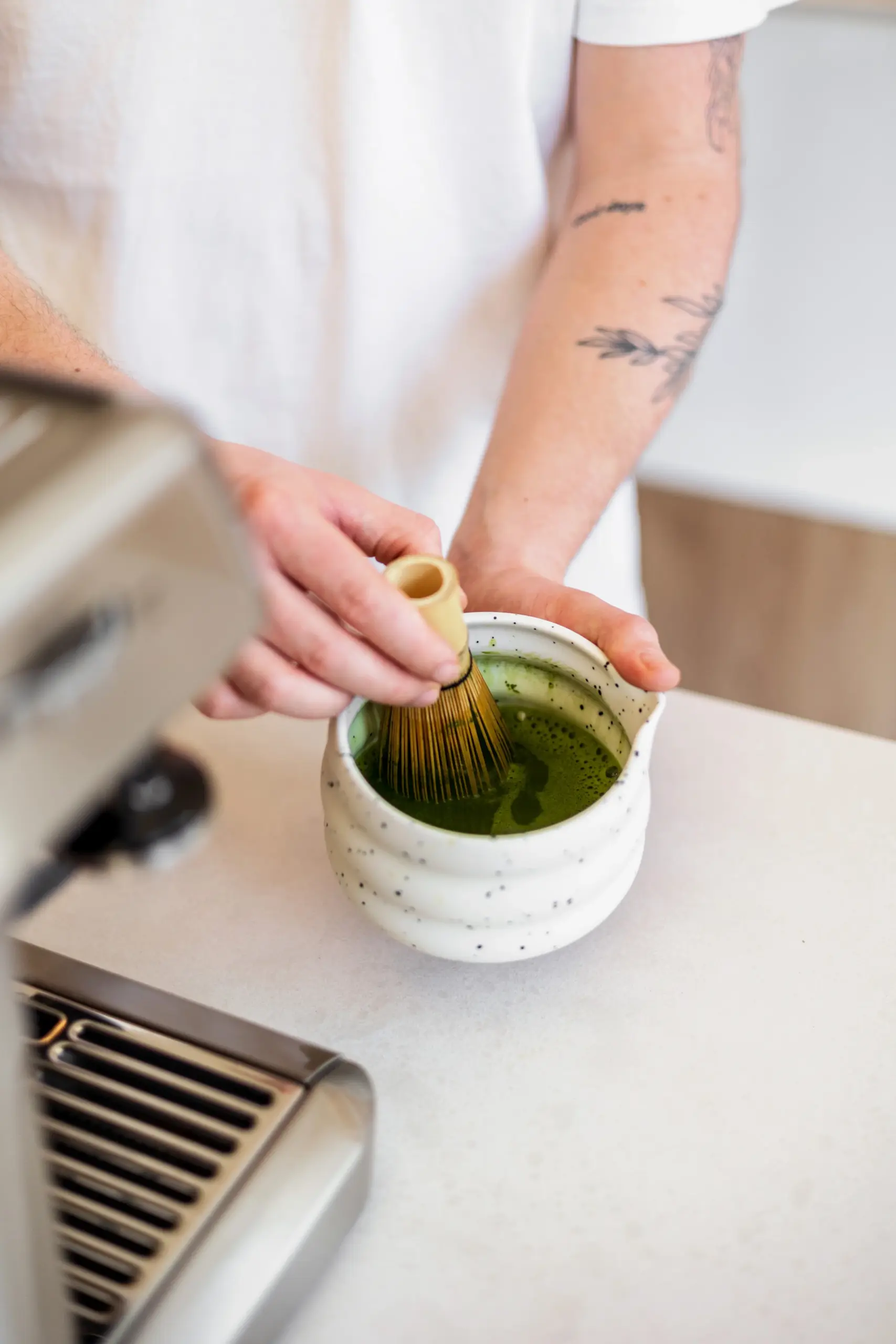 SHINYU matcha - Large pack 5 Person whisking matcha tea with a bamboo chasen in a speckled ceramic bowl on a counter
