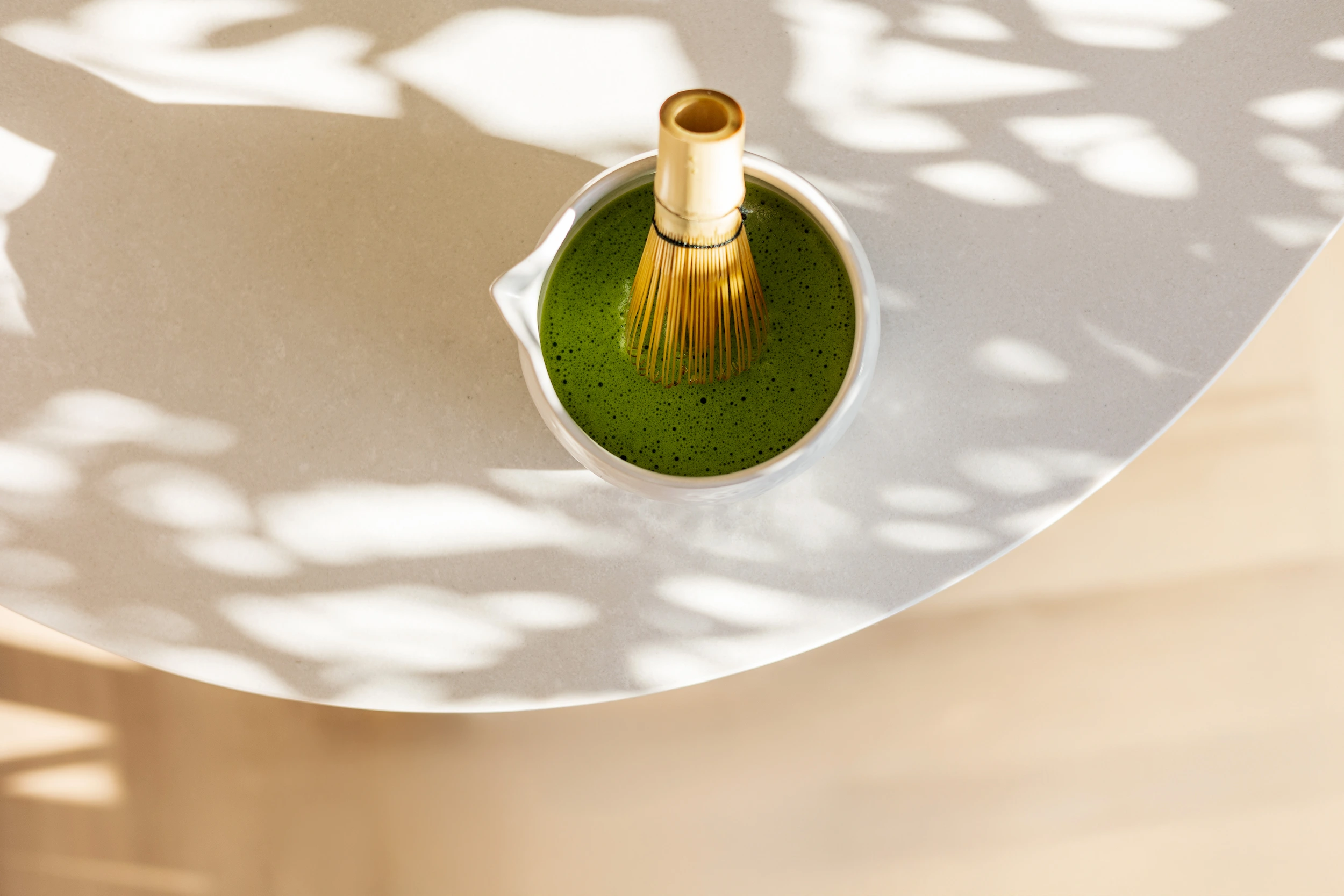 SHINYU Matcha Whisk 3 Witte kom met verse matcha en een bamboeklopper, van bovenaf gefotografeerd in zonlicht met bladschaduwen