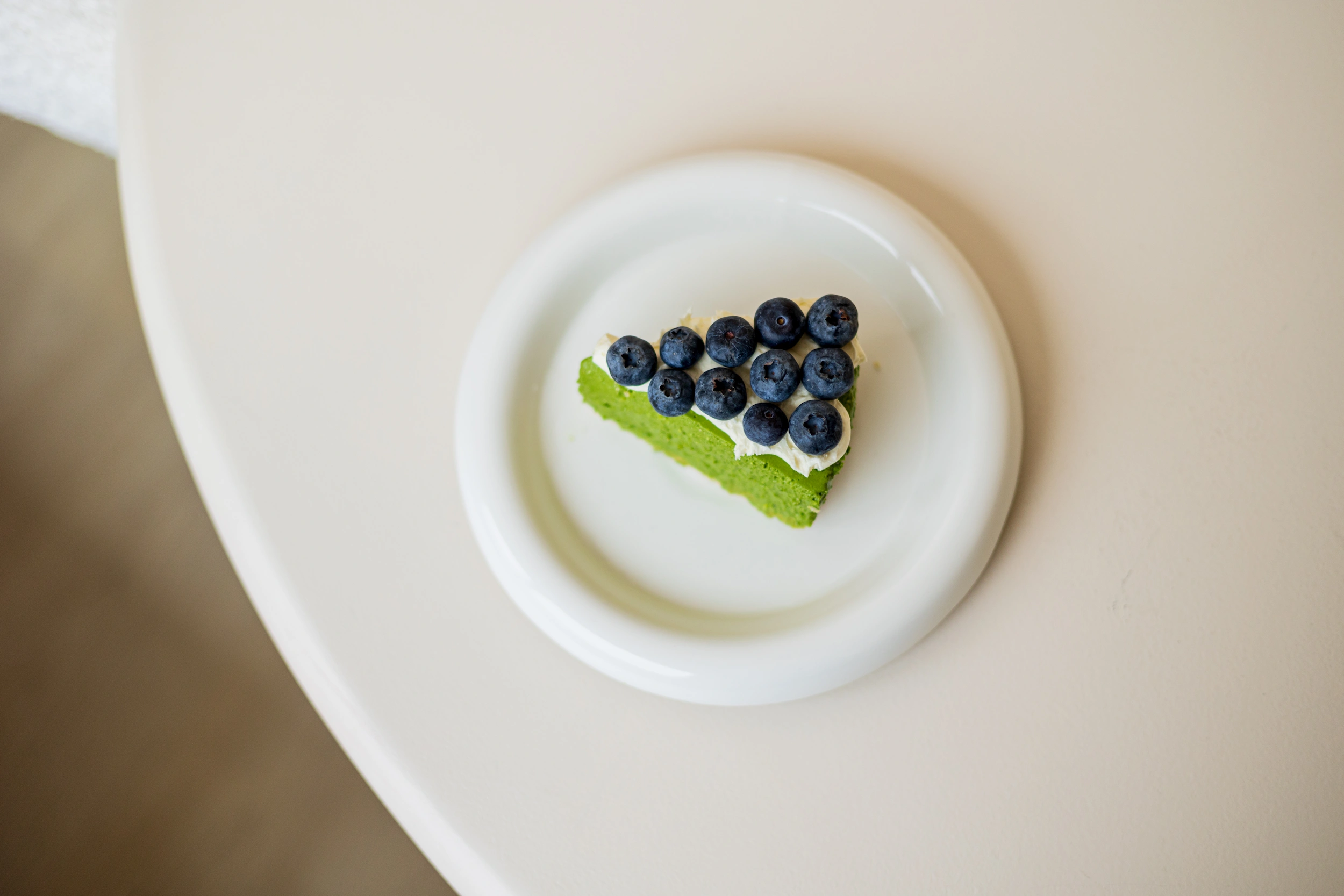 SHINYU Matcha - Bewaarblik 7 Punt groene matcha cake met slagroom en verse bosbessen op een wit bord, van bovenaf gefotografeerd