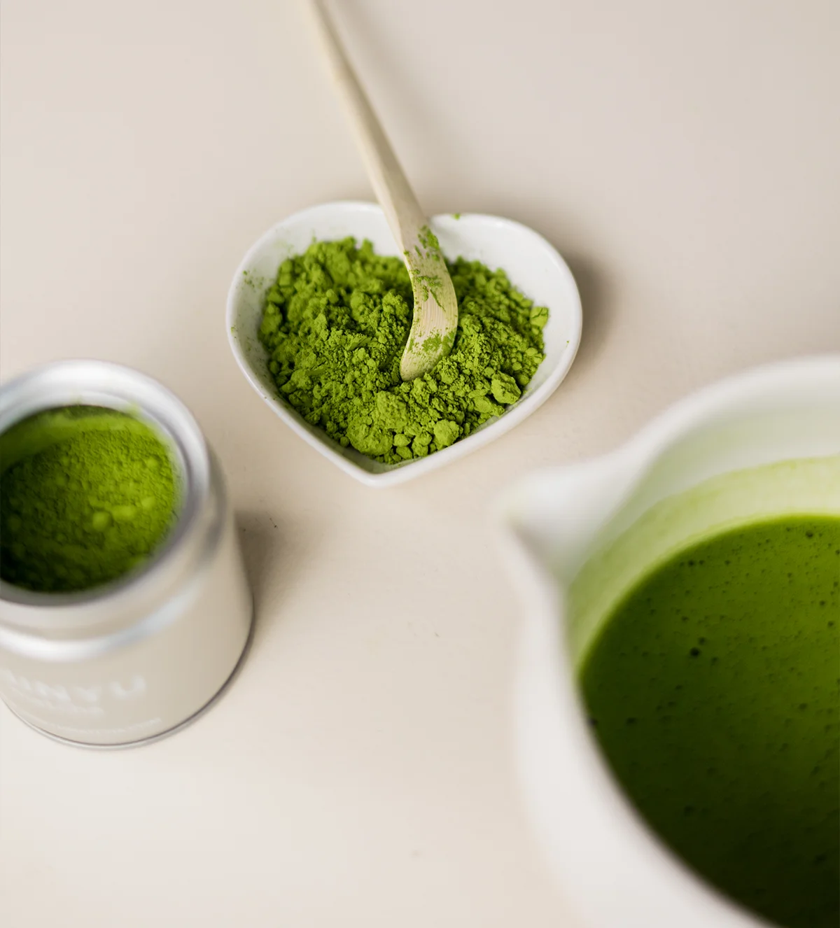 SHINYU Matcha - Bewaarblik 8 Matcha poeder in een hartvormig schaaltje met een bamboespatel, naast een blik matcha en een kopje matcha thee