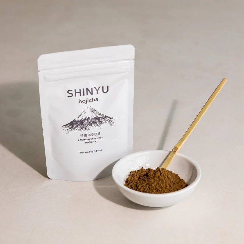 SHINYU Hojicha Triple Pack (3x30gr) 6 Shinyu Premium Japanese Hojicha powder in a white resealable bag, beside a small bowl of brown hojicha powder with a bamboo s