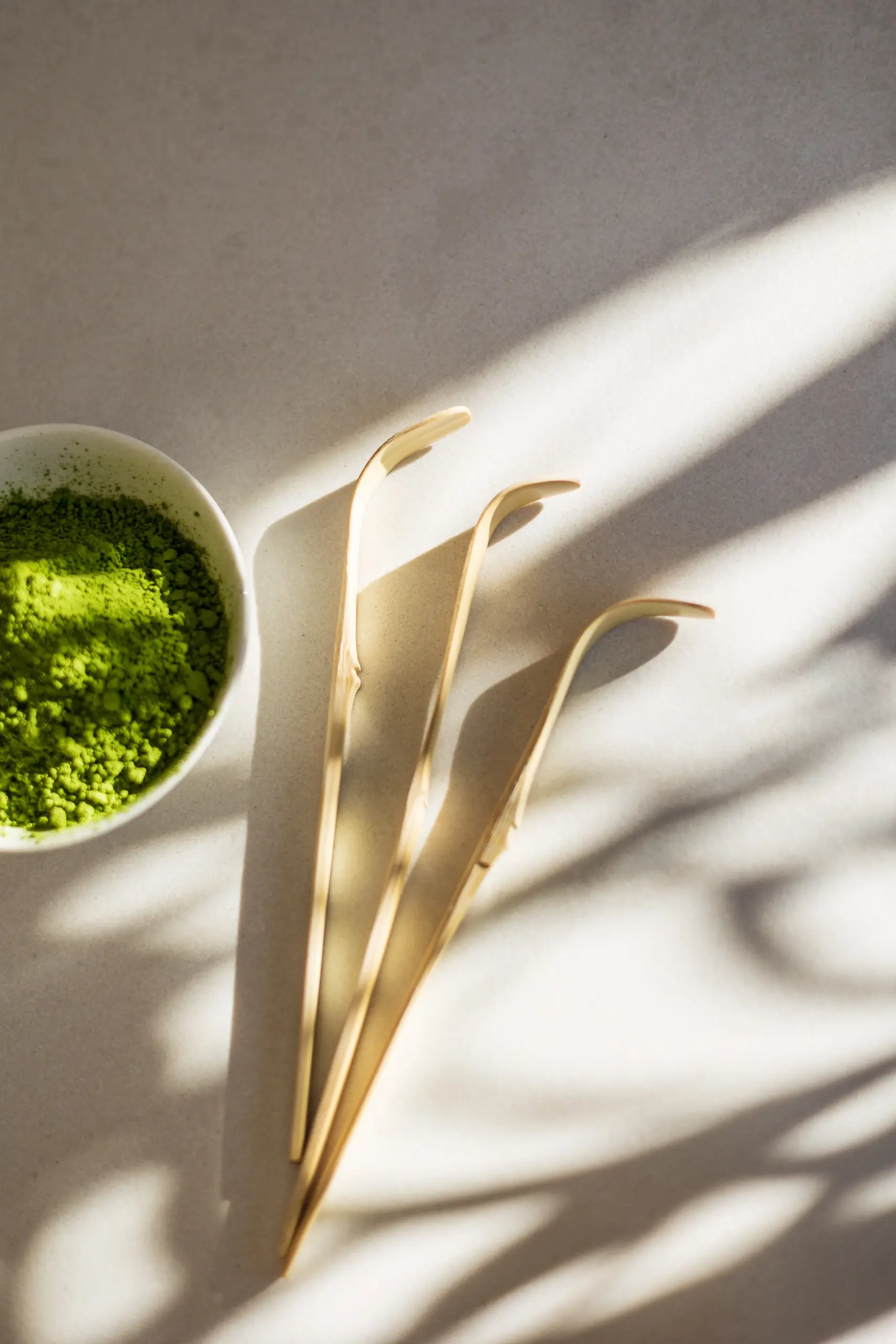 Voordeelbundel (triple pack matcha + whisk + lepel) 4 Kommetje met matcha-poeder naast drie bamboe matcha-lepeltjes in zonlicht
